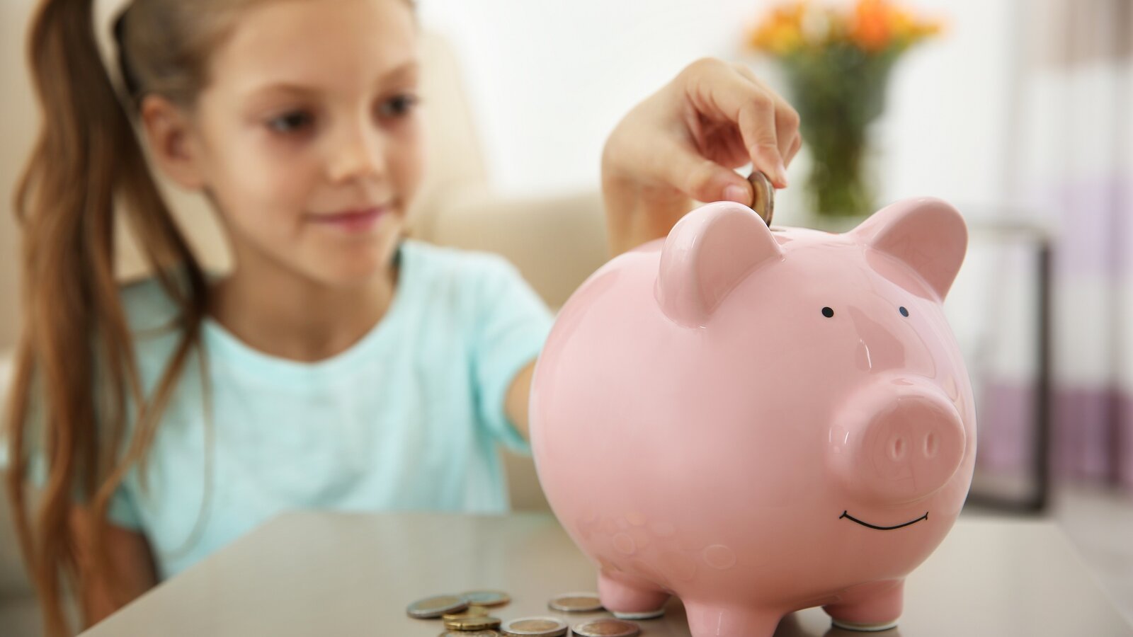 Ein Mädchen steckt ihr Taschengeld in ein Sparschwein. Wie viel sollten Kinder bekommen?